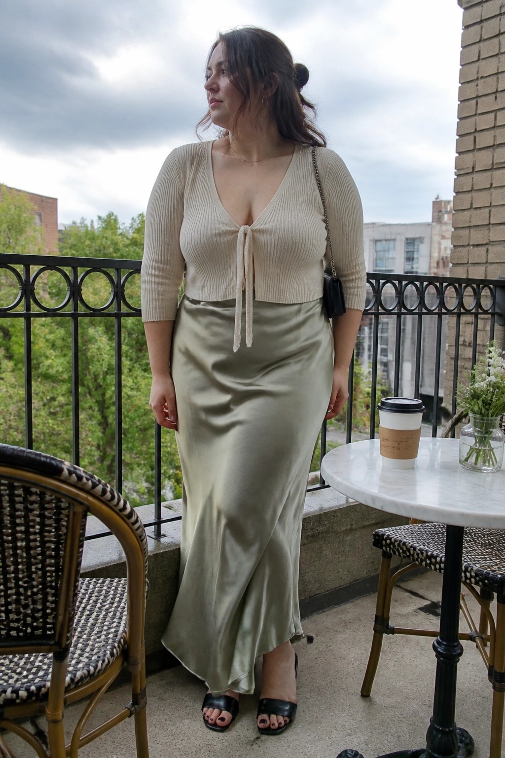 Woman in beige tie-front crop top and sage satin skirt on balcony