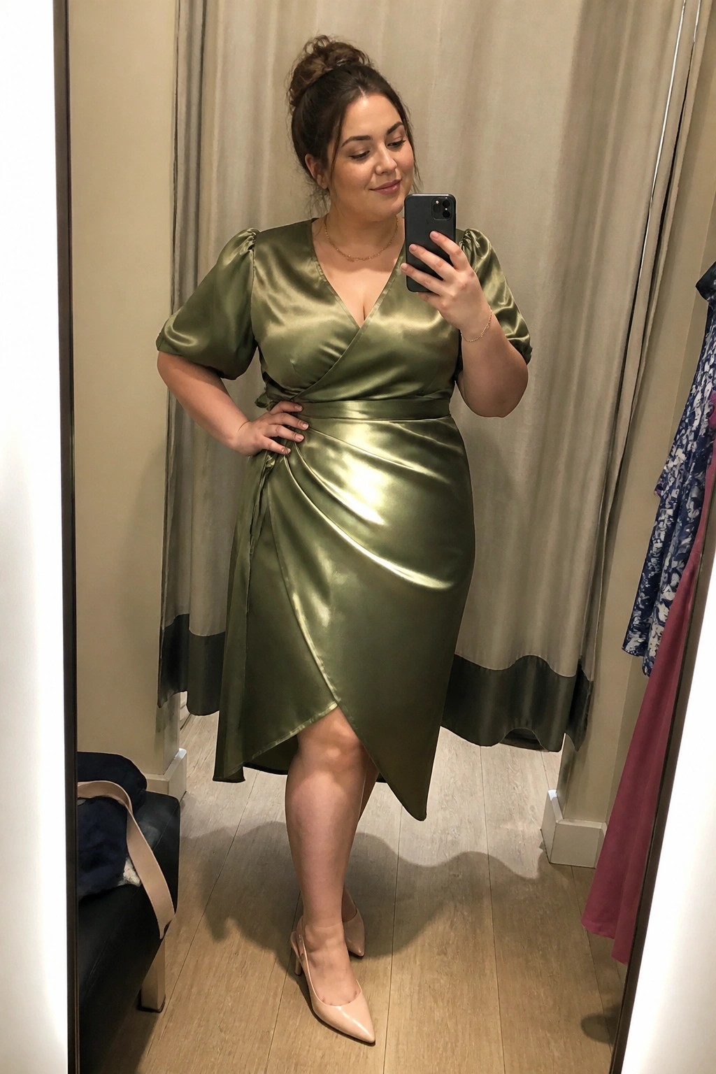 Woman in olive green satin wrap dress taking mirror selfie in fitting room