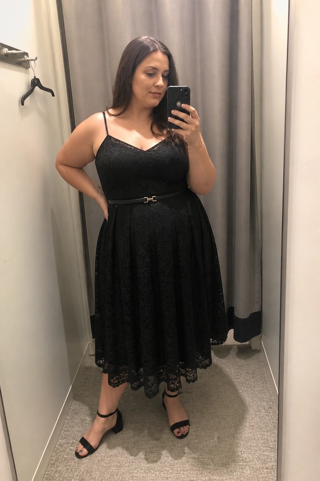 Woman in black lace dress taking mirror selfie in fitting room