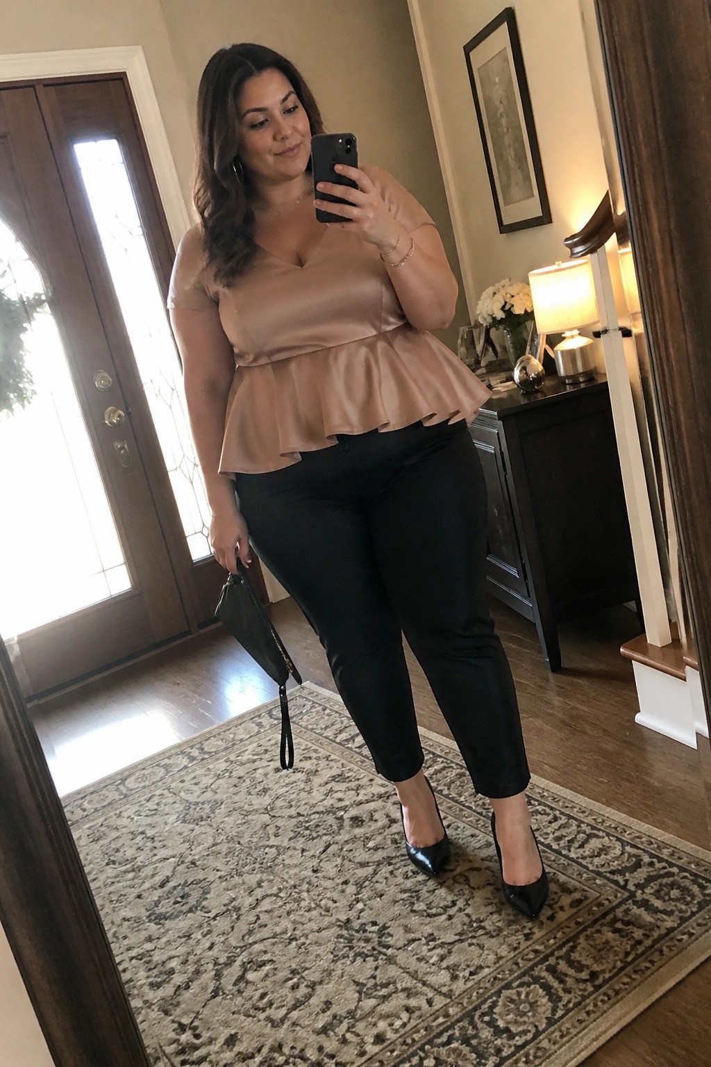 Woman in beige peplum top and black pants taking mirror selfie with phone