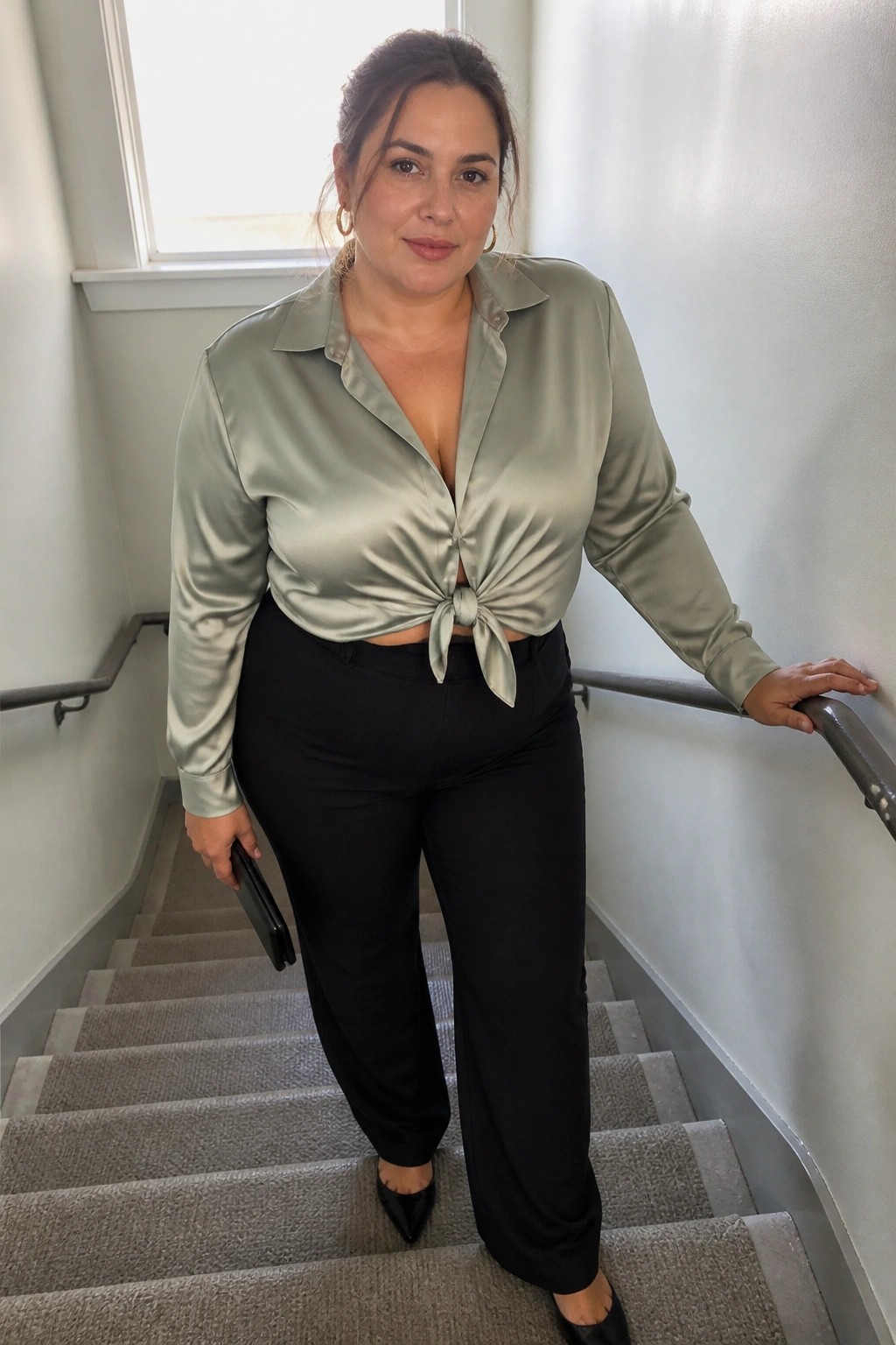 Woman in sage green satin blouse tied at waist on carpeted stairs