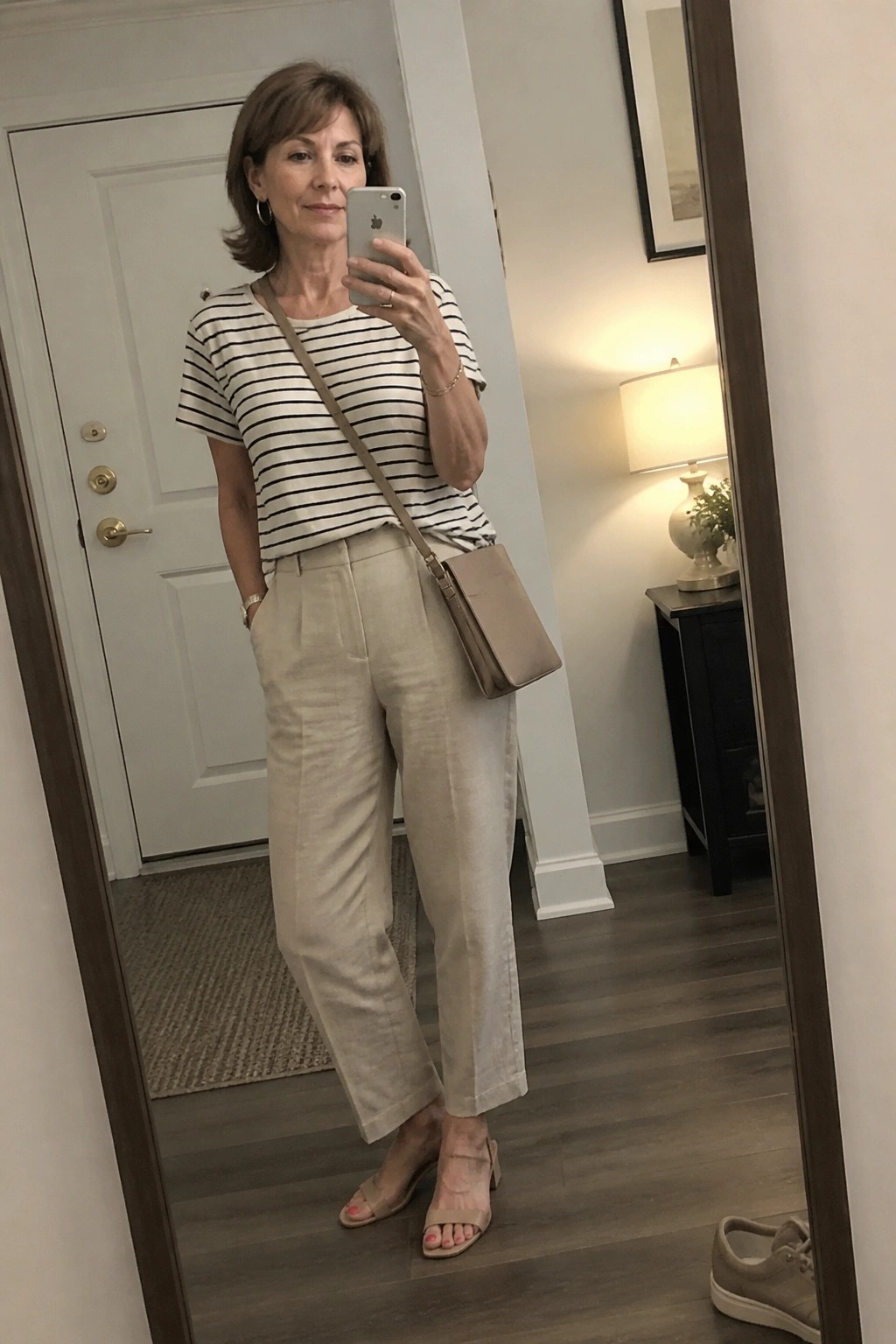 Woman in striped shirt and beige pants taking mirror selfie with phone