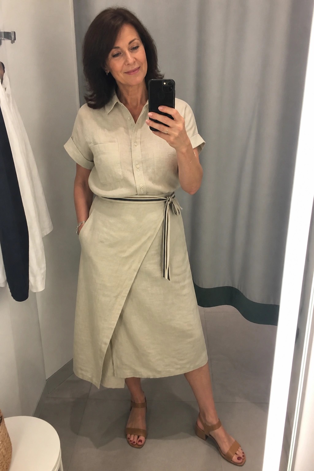 Woman in light green linen shirt and wrap skirt taking mirror selfie in fitting room