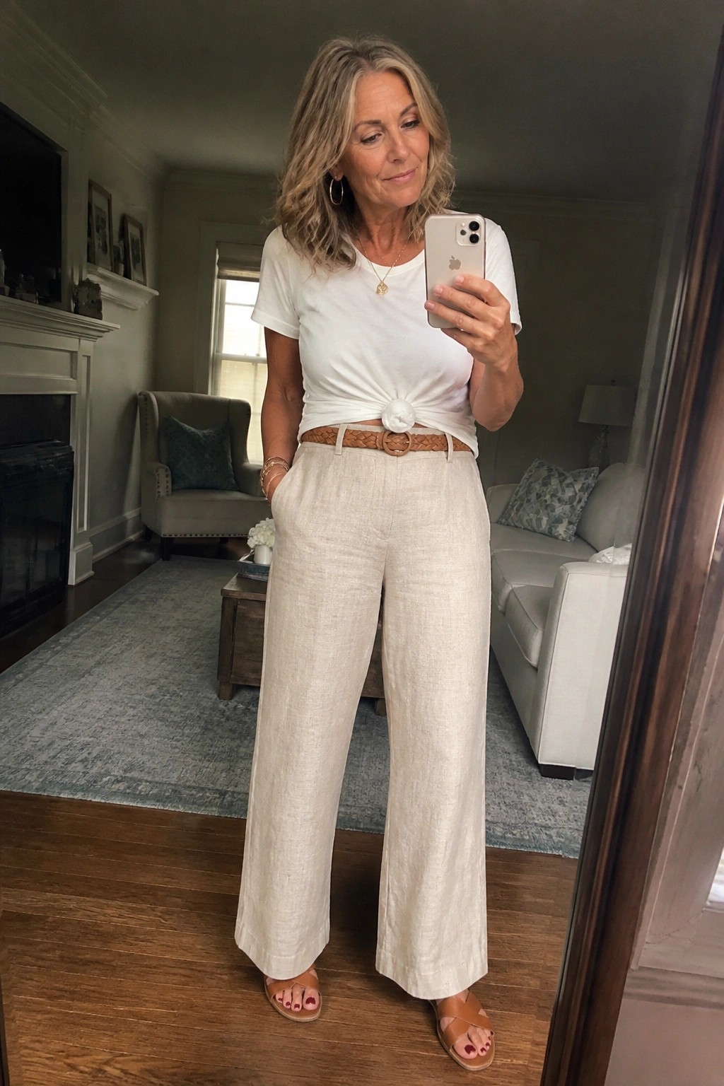 Gray-haired woman in white knotted tee and beige wide-leg pants taking mirror selfie