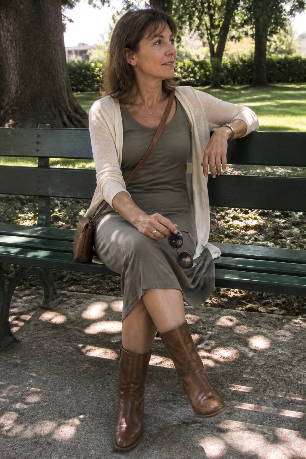 Woman in gray dress and cream cardigan on green park bench with brown boots