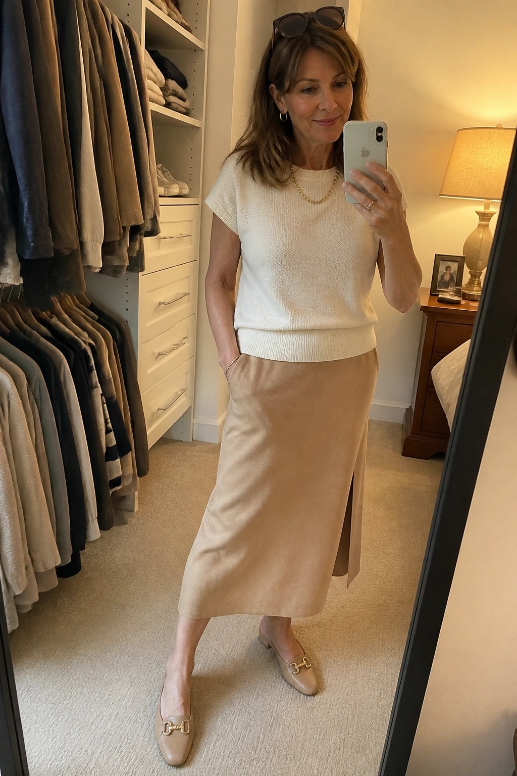 Woman in cream knit top and beige skirt taking mirror selfie in closet
