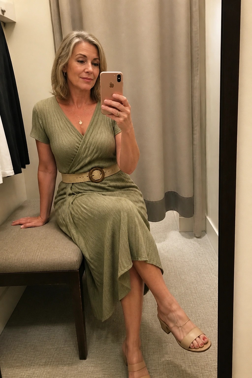 Woman in sage green wrap dress taking mirror selfie in fitting room