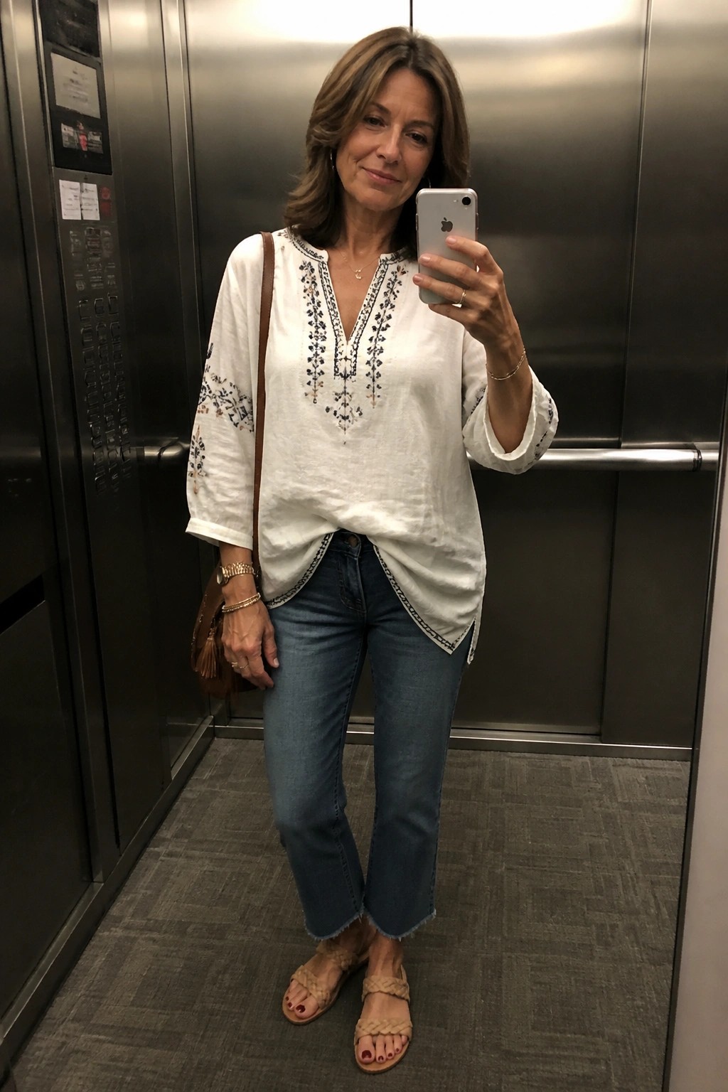 Woman in white embroidered blouse and jeans taking selfie in elevator