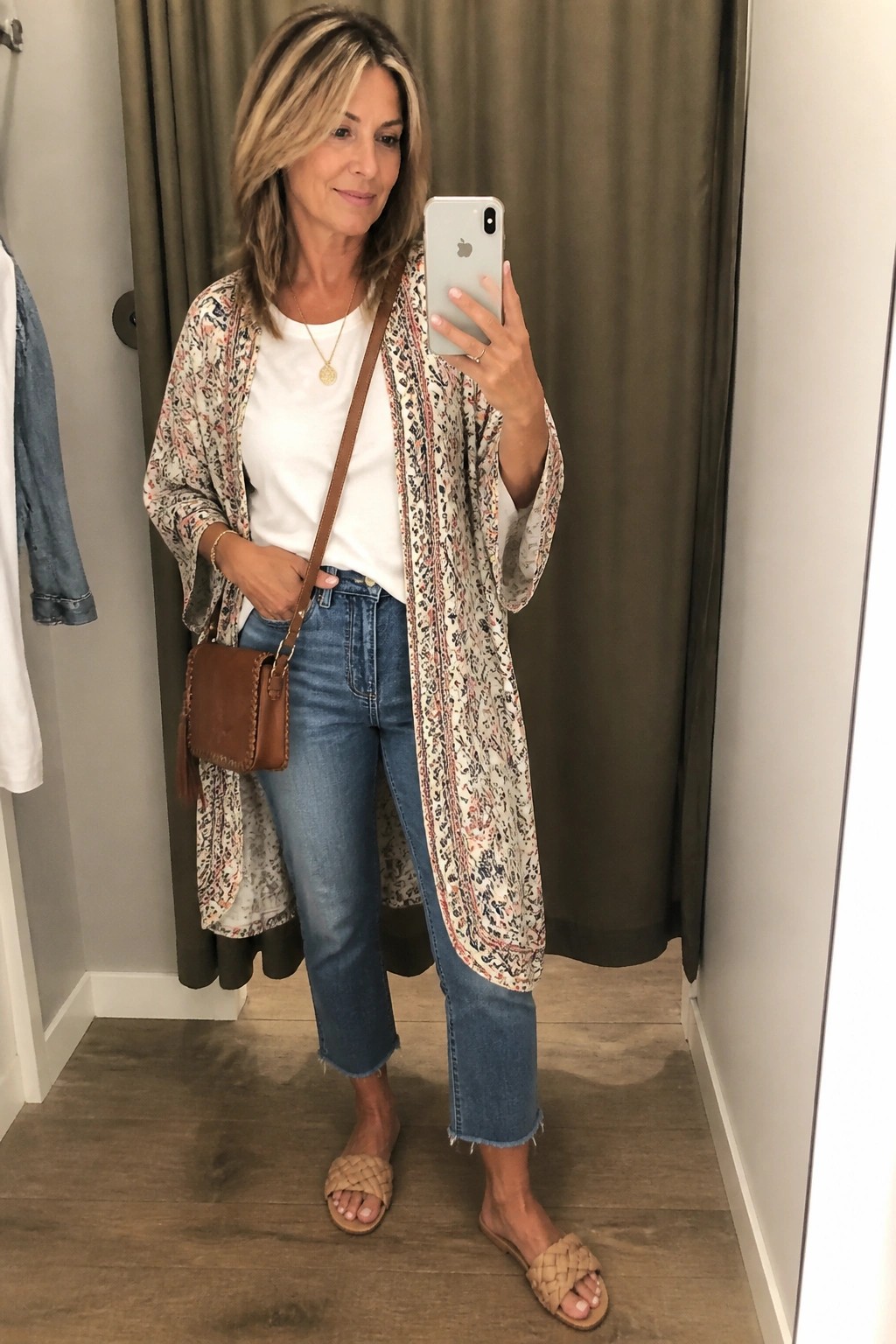 Woman in floral kimono duster, white tee, and jeans taking mirror selfie.