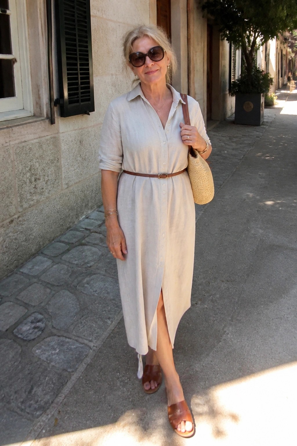 Older woman in beige linen shirt dress with brown belt on cobblestone street