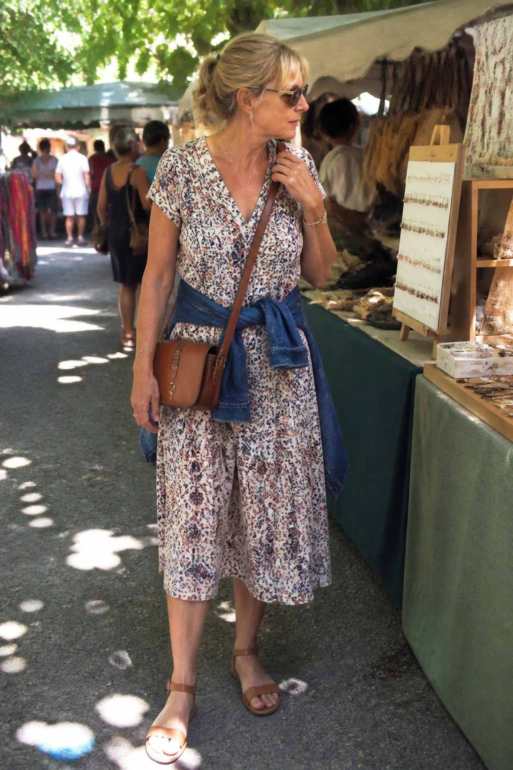 Woman in floral dress with denim tied at waist beside jewelry display at market