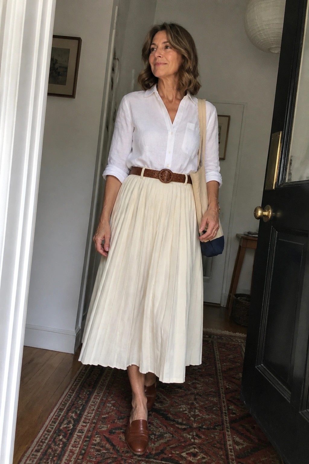 Woman in white shirt, cream pleated skirt, brown belt and loafers with tote bag