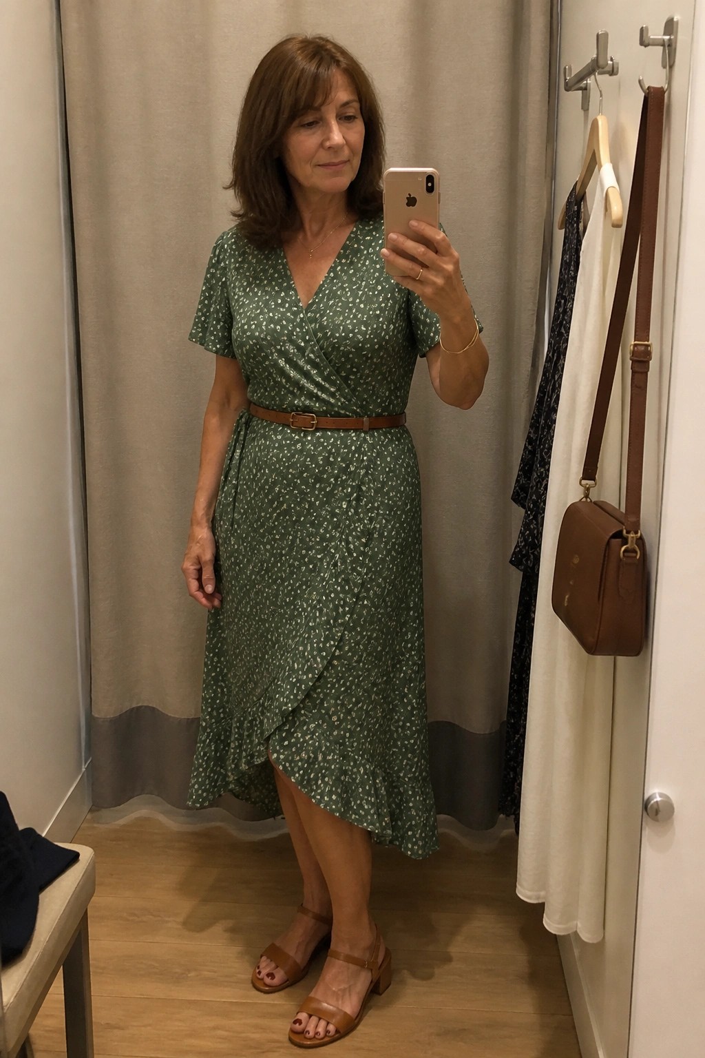 Woman in green floral wrap dress taking mirror selfie in fitting room