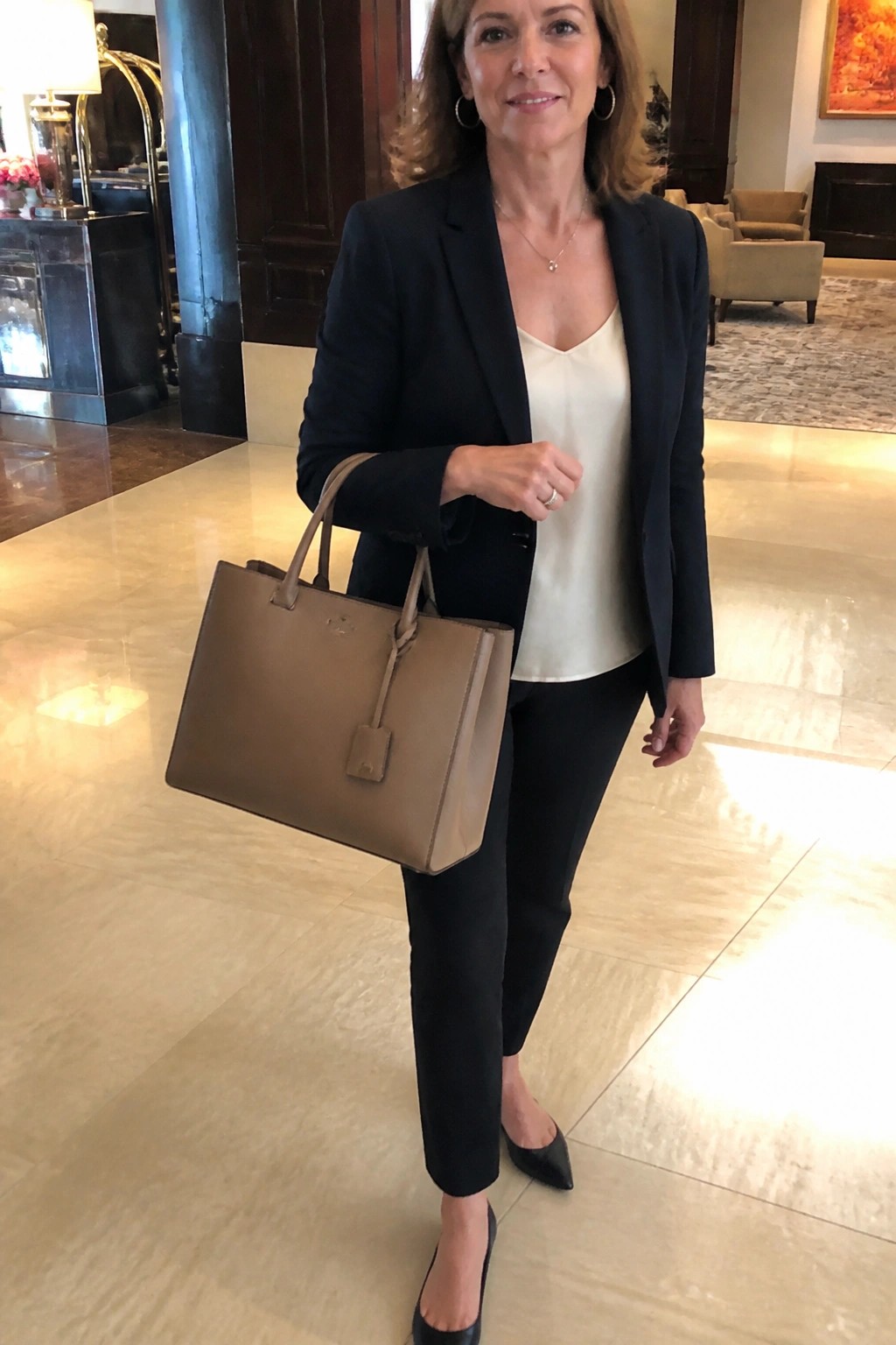 Businesswoman in black blazer holding beige tote bag in marble lobby