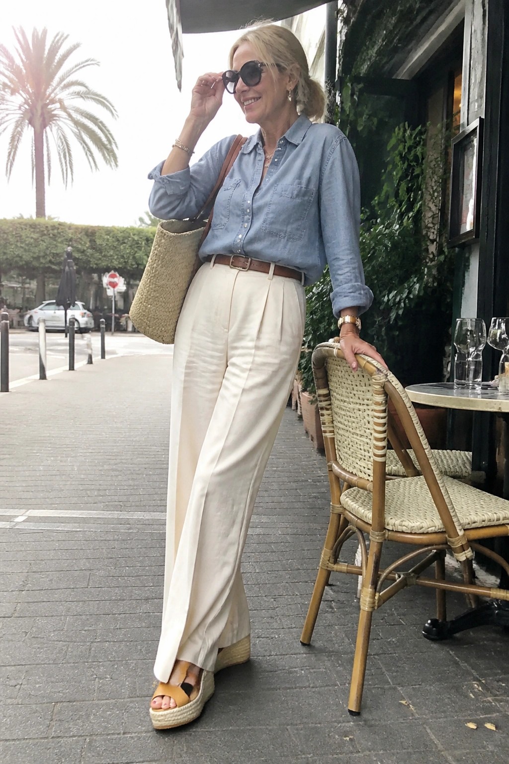 Blonde woman in blue denim shirt and white pants at outdoor cafe