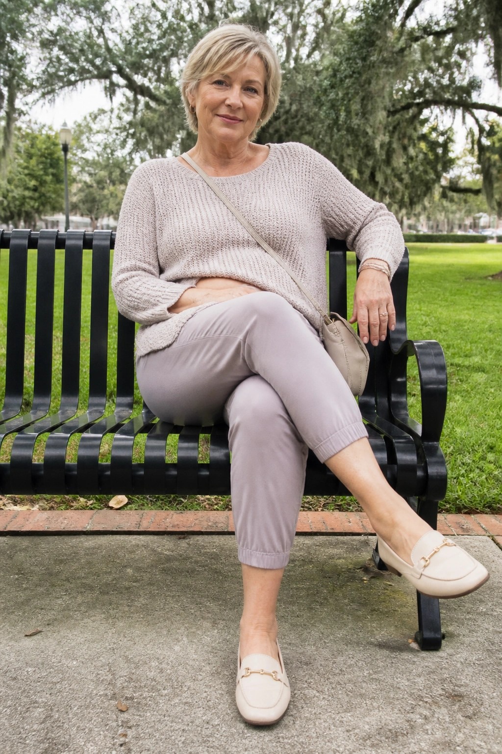 Elderly woman with short gray hair in beige sweater sits on black park bench