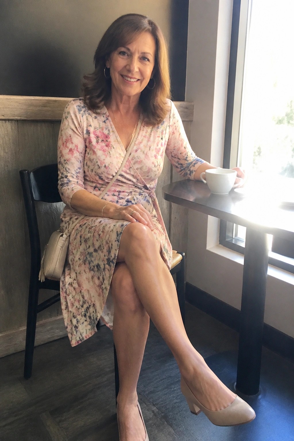 Woman in floral wrap dress smiling at cafe table by sunny window