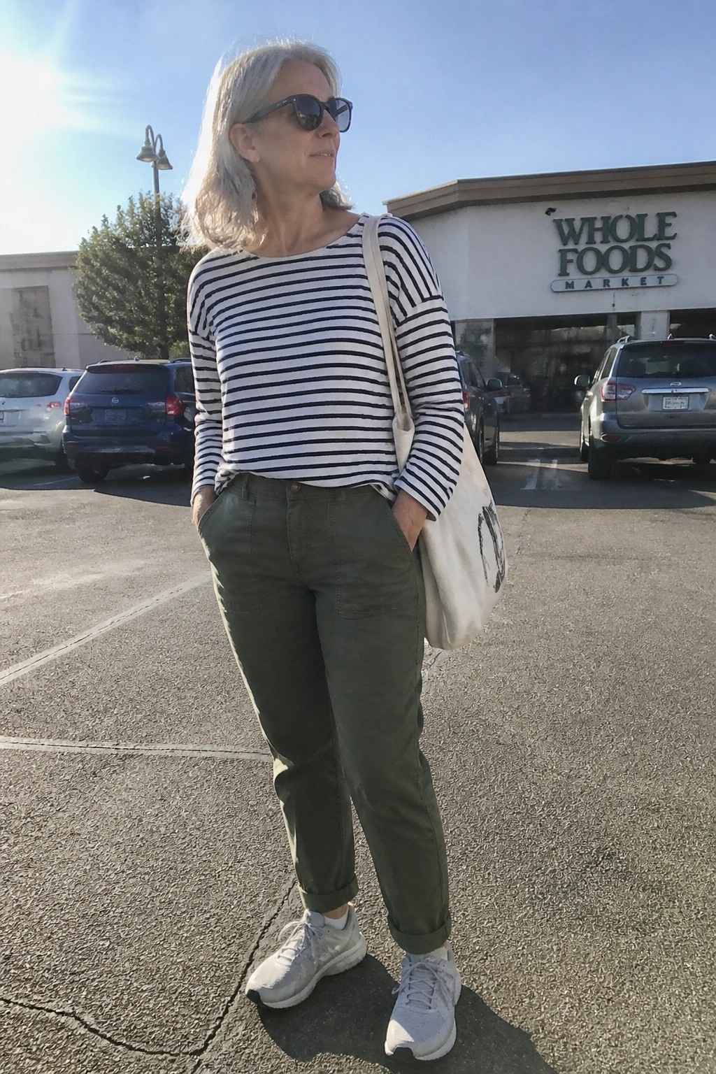 Gray-haired woman in striped shirt and green pants with tote bag in parking lot