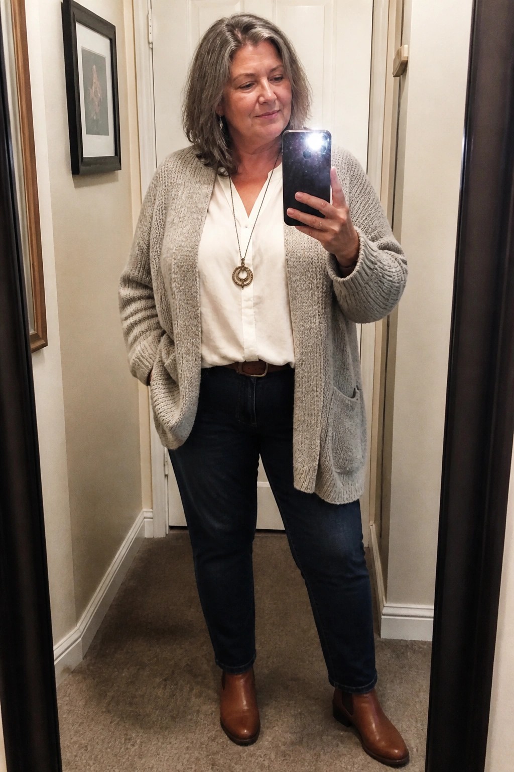 Woman in beige cardigan and jeans taking mirror selfie with smartphone