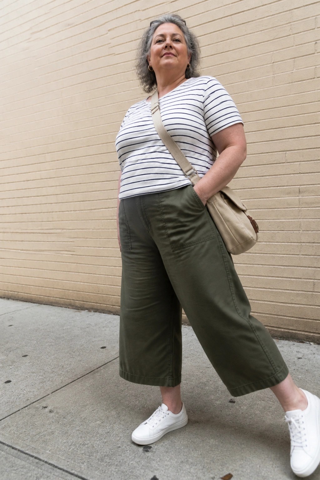 Woman with gray curls in striped top and olive pants by brick wall