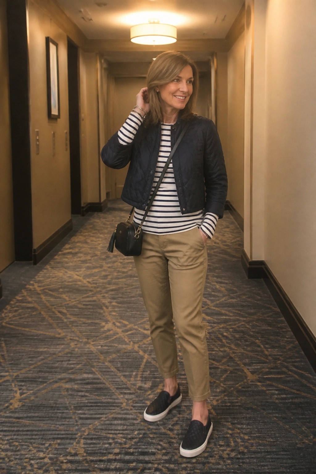 Woman in navy quilted jacket and striped shirt with black bag in hallway