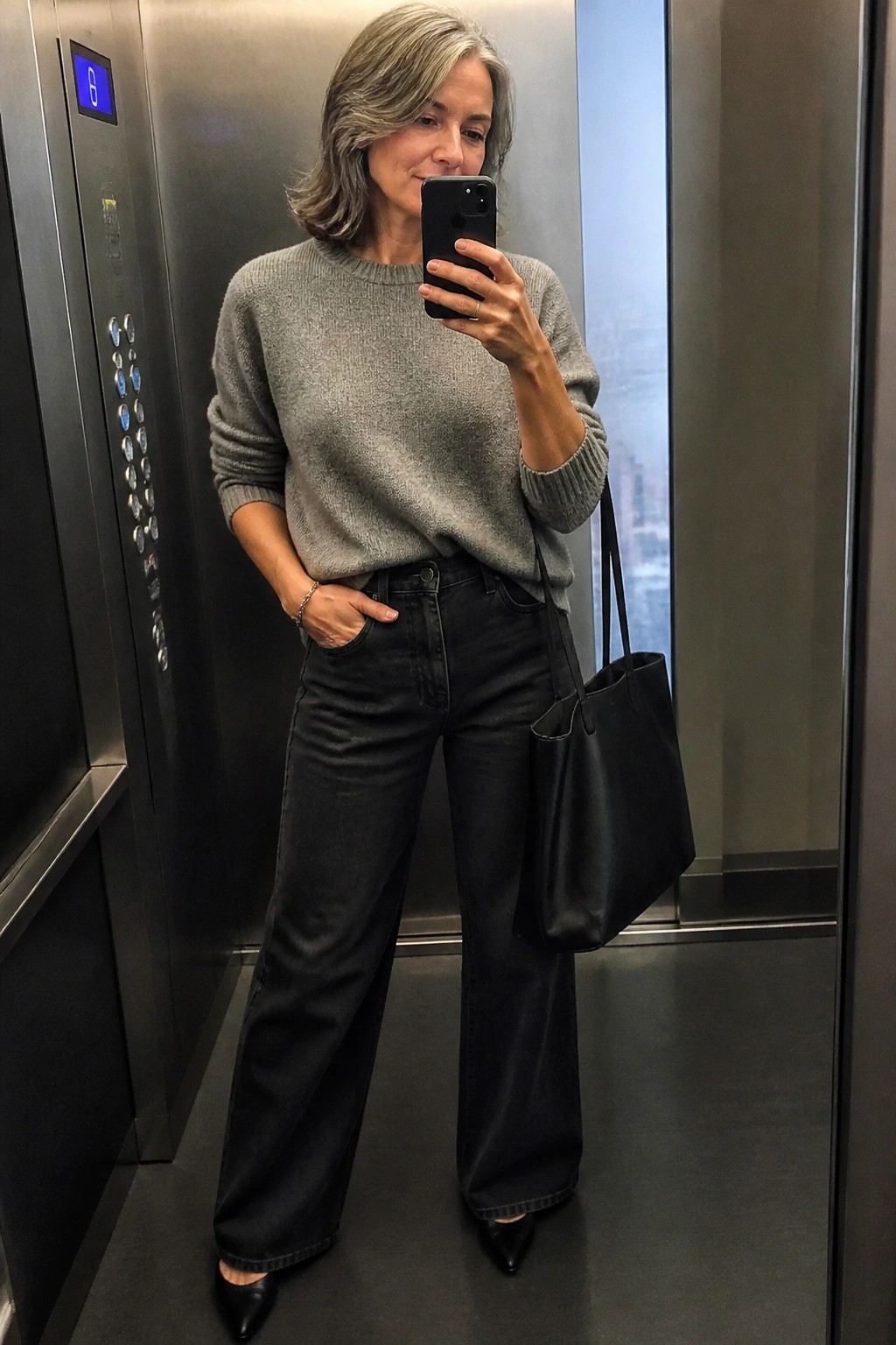 Woman in gray sweater and black wide-leg jeans taking selfie in elevator