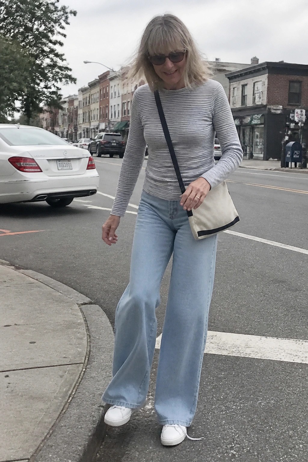 Woman in striped top and light blue wide-leg jeans with crossbody bag on street