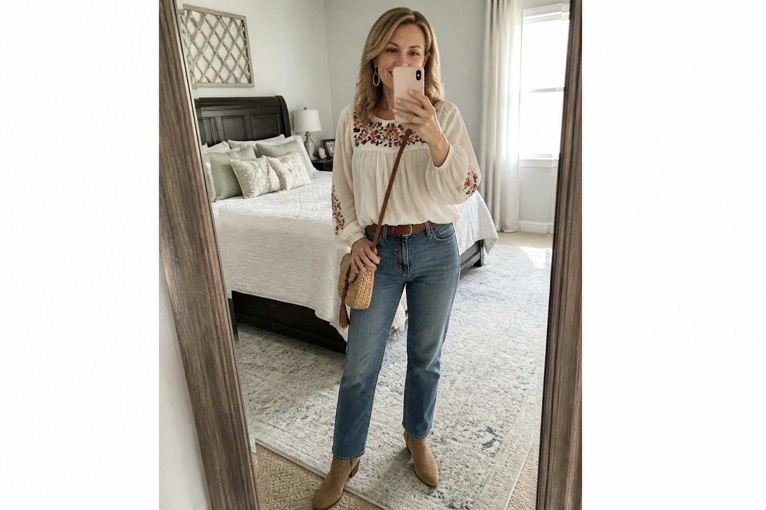 Woman in embroidered white blouse and blue jeans taking mirror selfie in bedroom