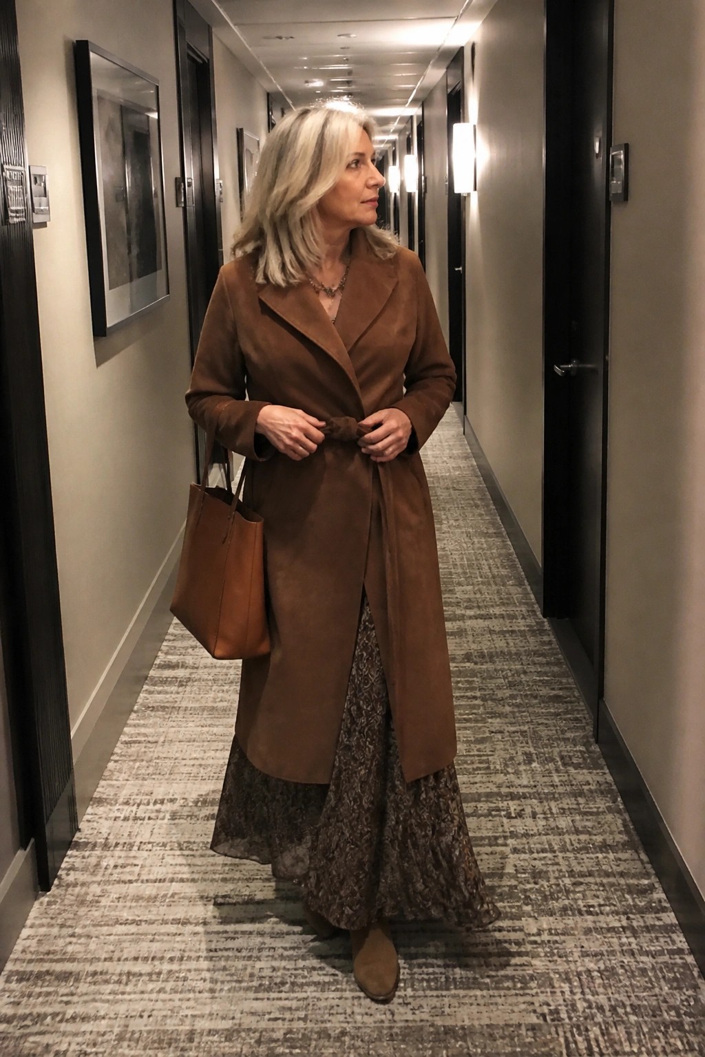 Woman in brown suede coat carrying leather tote in hotel hallway