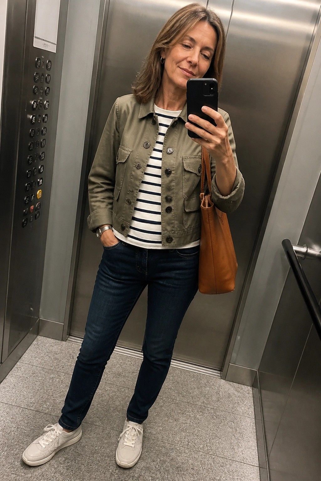 Woman in green jacket taking selfie in elevator wearing striped top and jeans