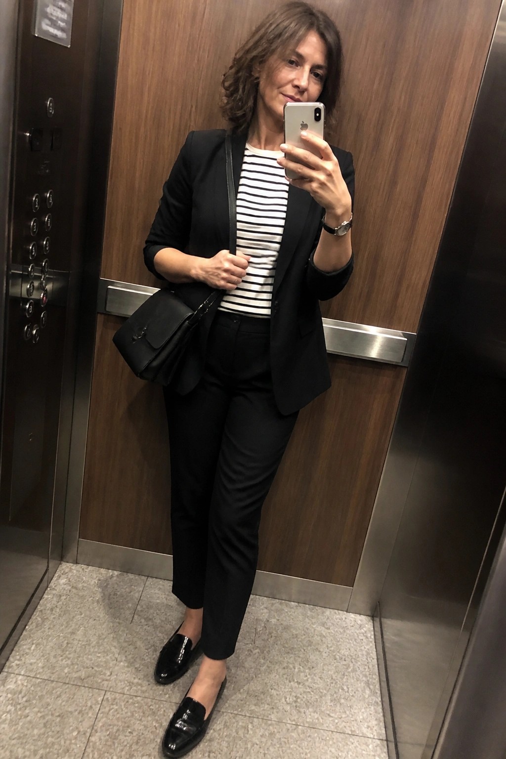 Woman in black blazer and striped shirt taking selfie in elevator