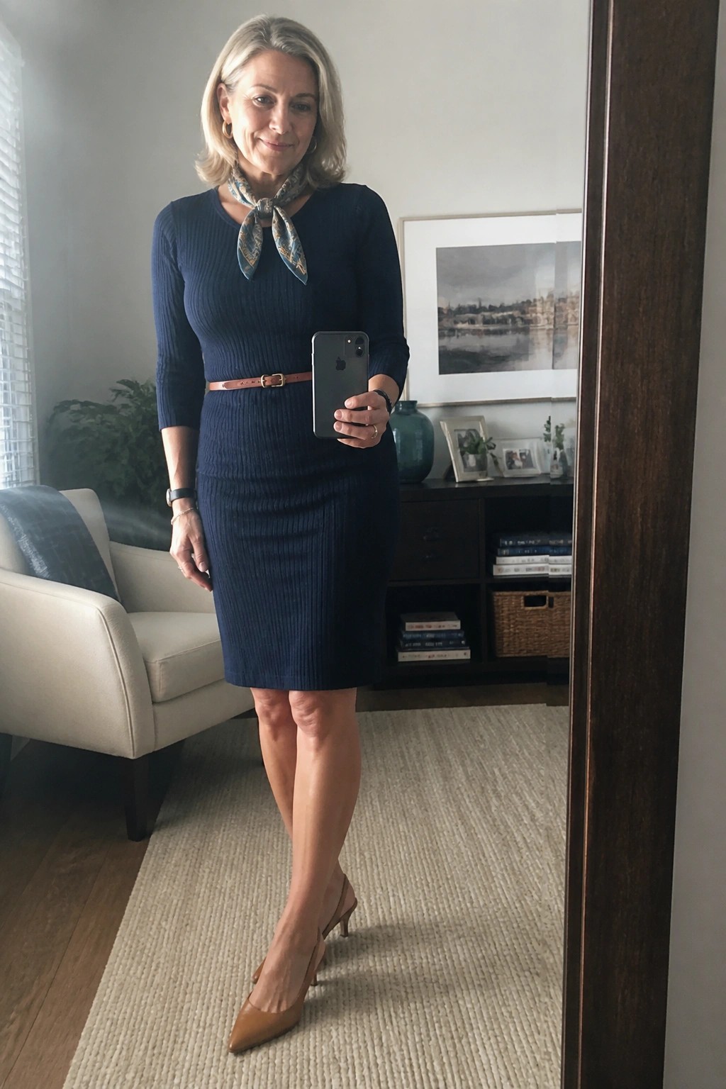 Woman in navy ribbed dress with scarf and brown belt holding smartphone indoors