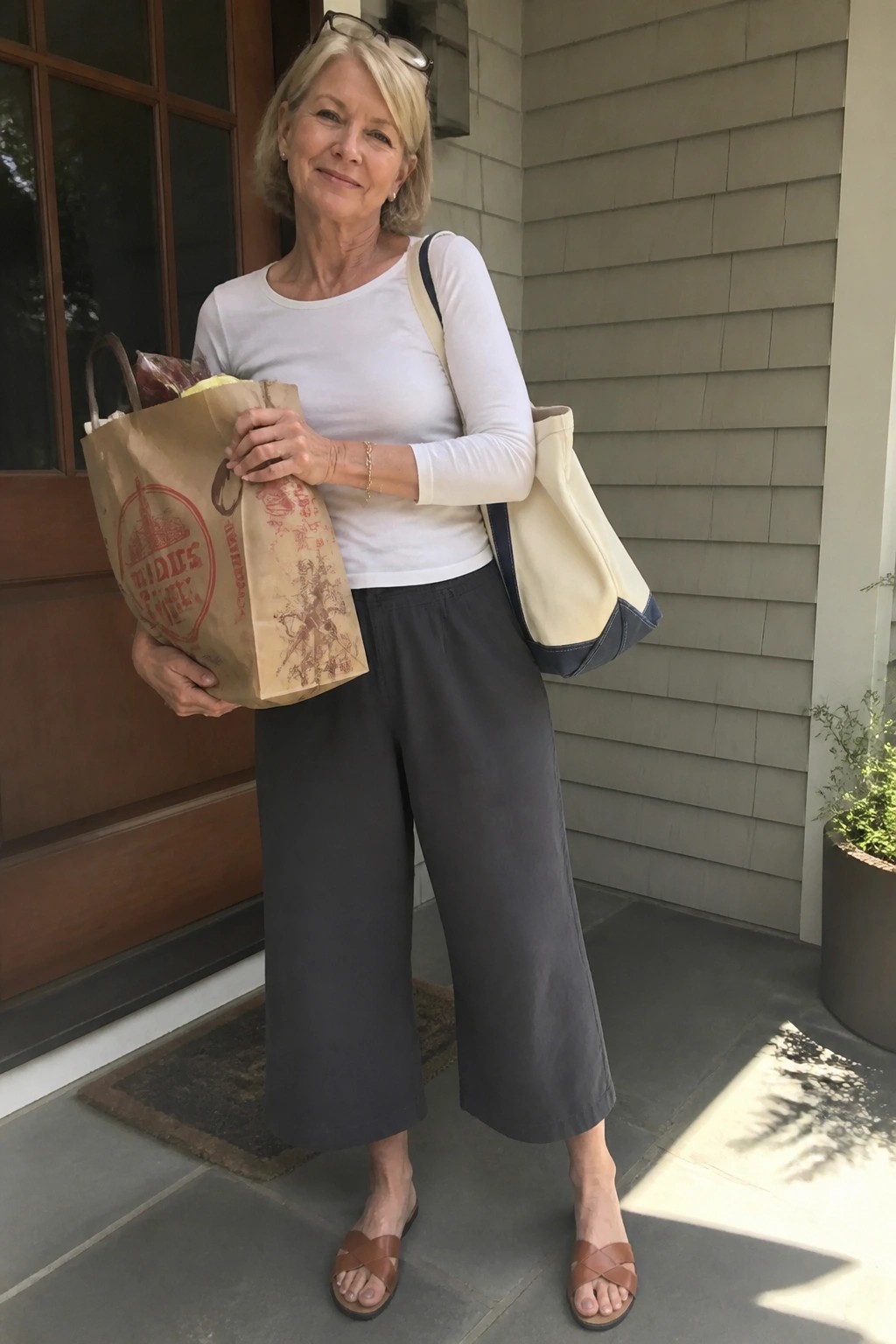 Older woman in white top and gray pants holding Trader Joe's grocery bag on porch
