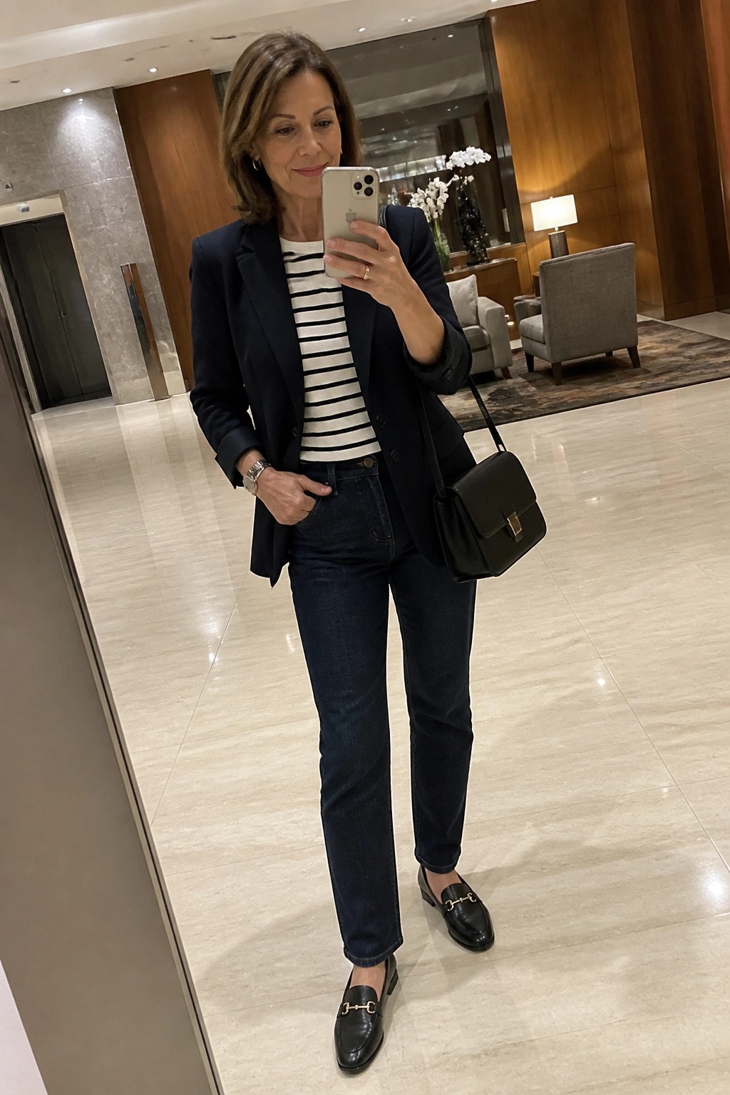 Woman in navy blazer and jeans taking mirror selfie in elegant lobby