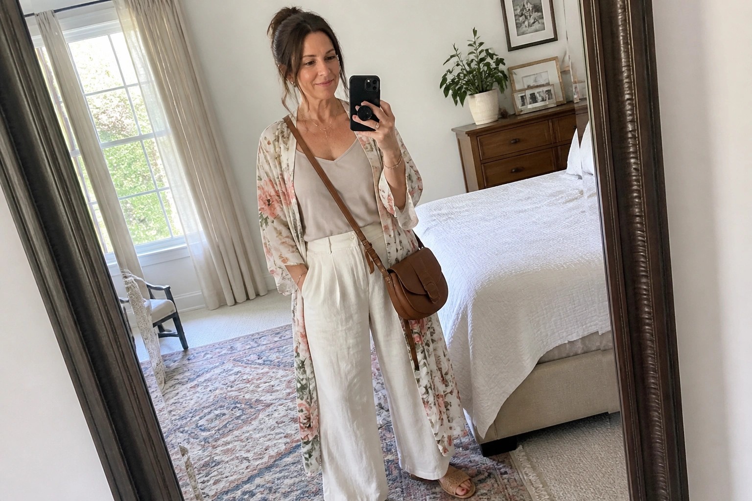 Woman in white linen and floral kimono taking mirror selfie with brown bag.
