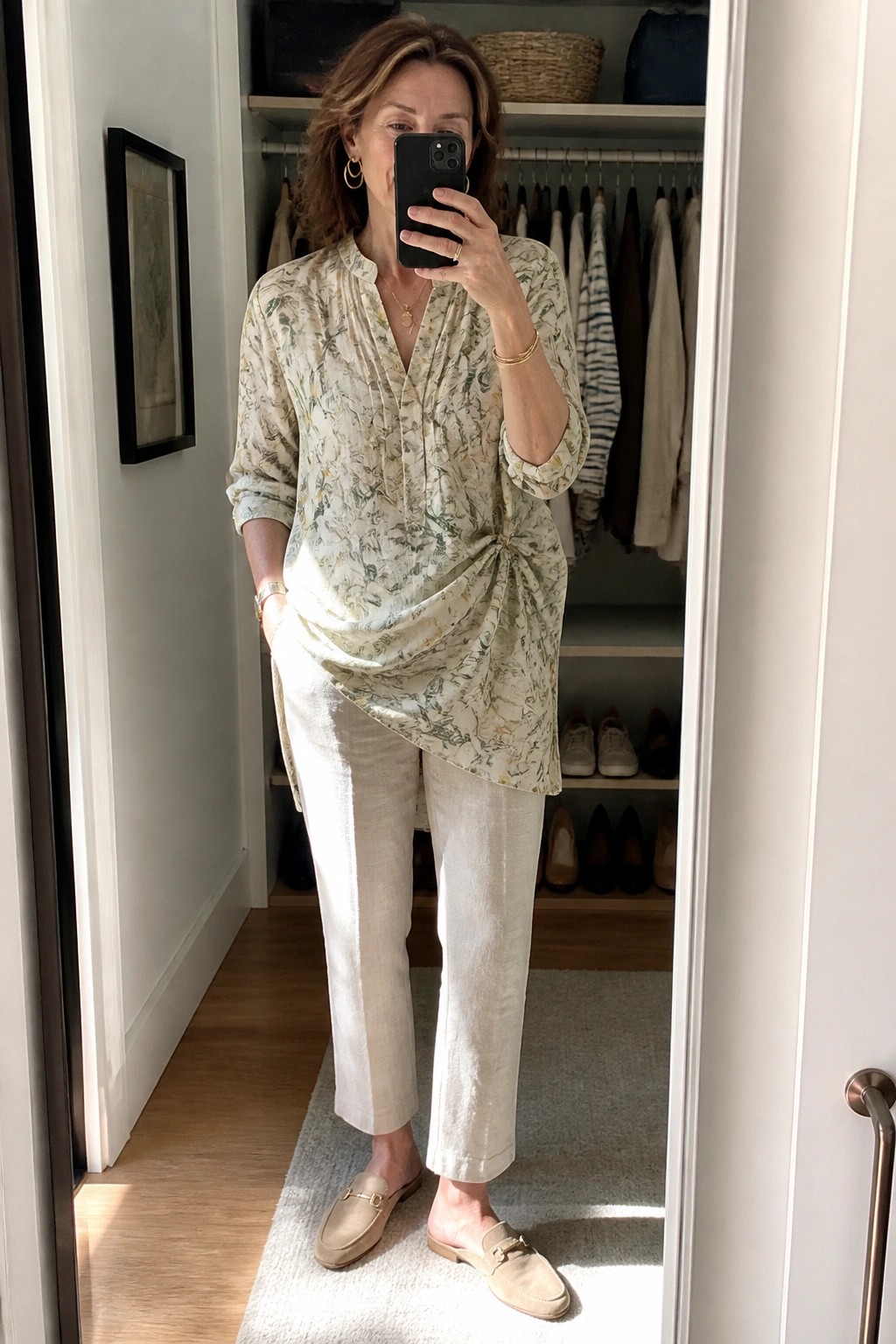 Woman in floral blouse and beige pants taking mirror selfie in closet