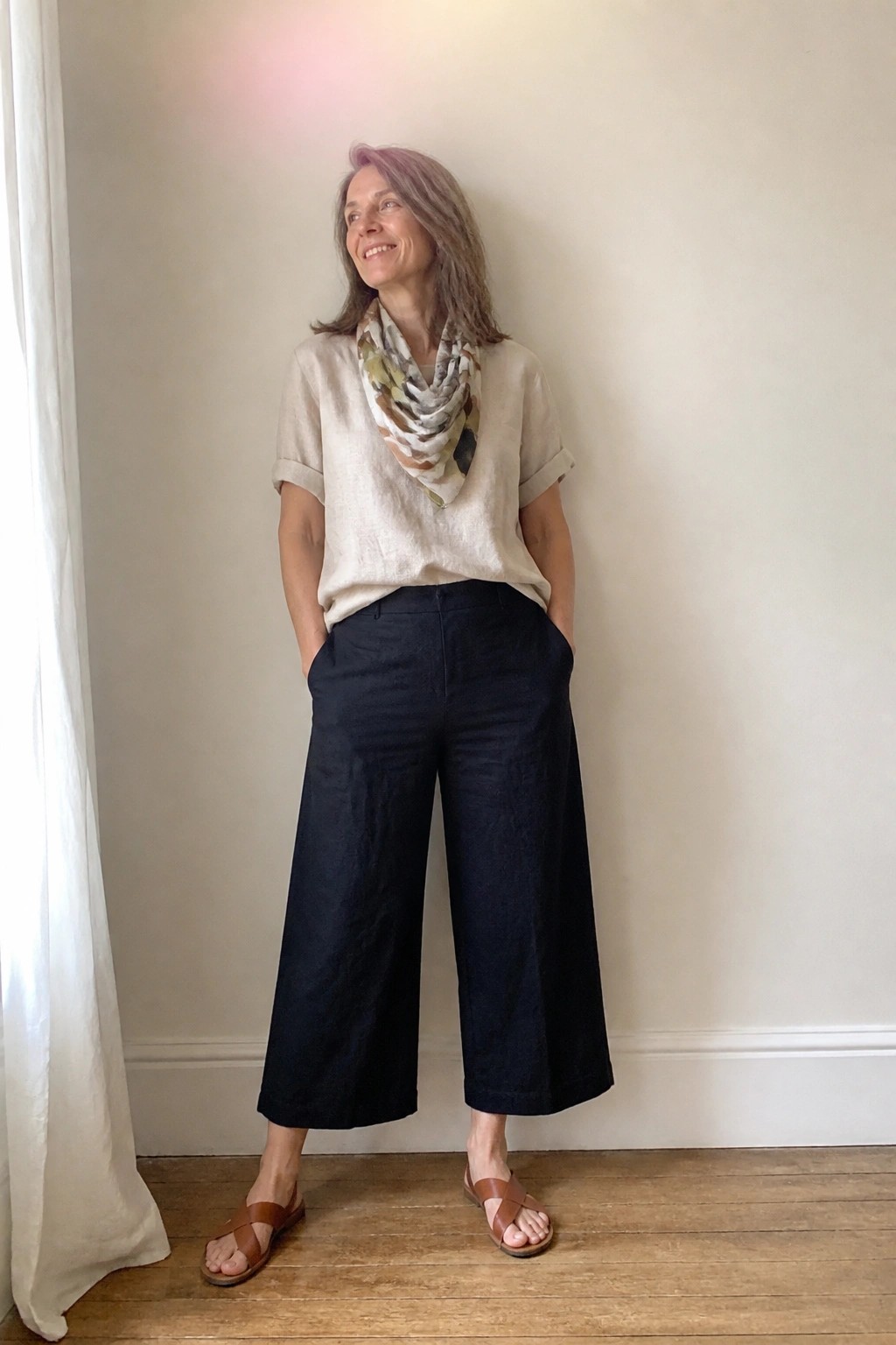 Woman in beige top, navy wide-leg pants, patterned scarf, and sandals.