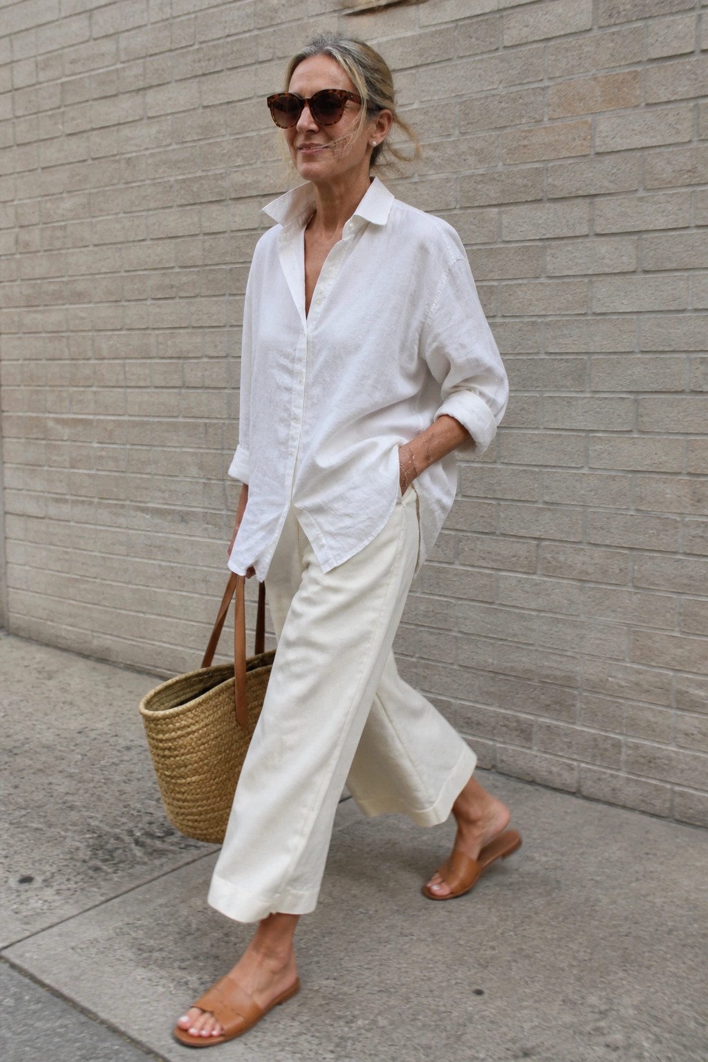 Woman in white shirt and wide pants holding woven straw bag on sidewalk
