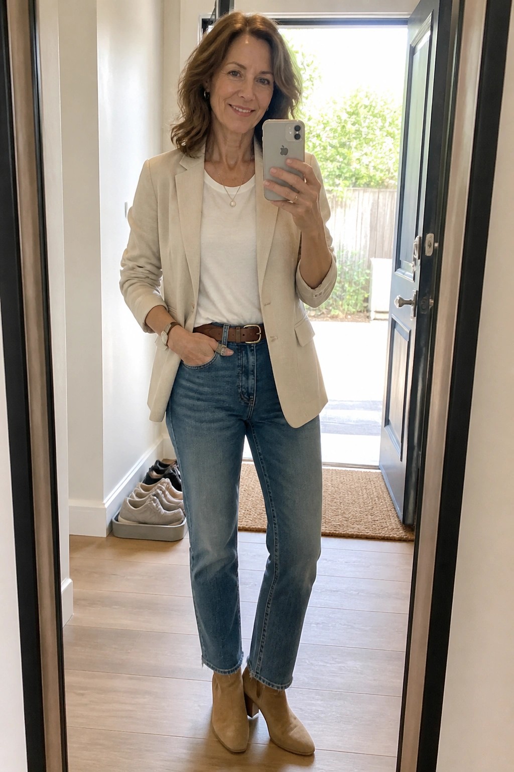 Woman in beige blazer and jeans taking mirror selfie in entryway