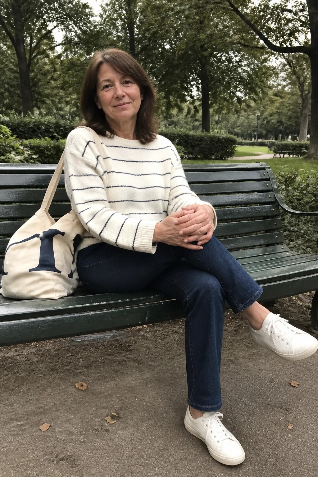 Woman in striped sweater and jeans on green park bench beside canvas tote bag