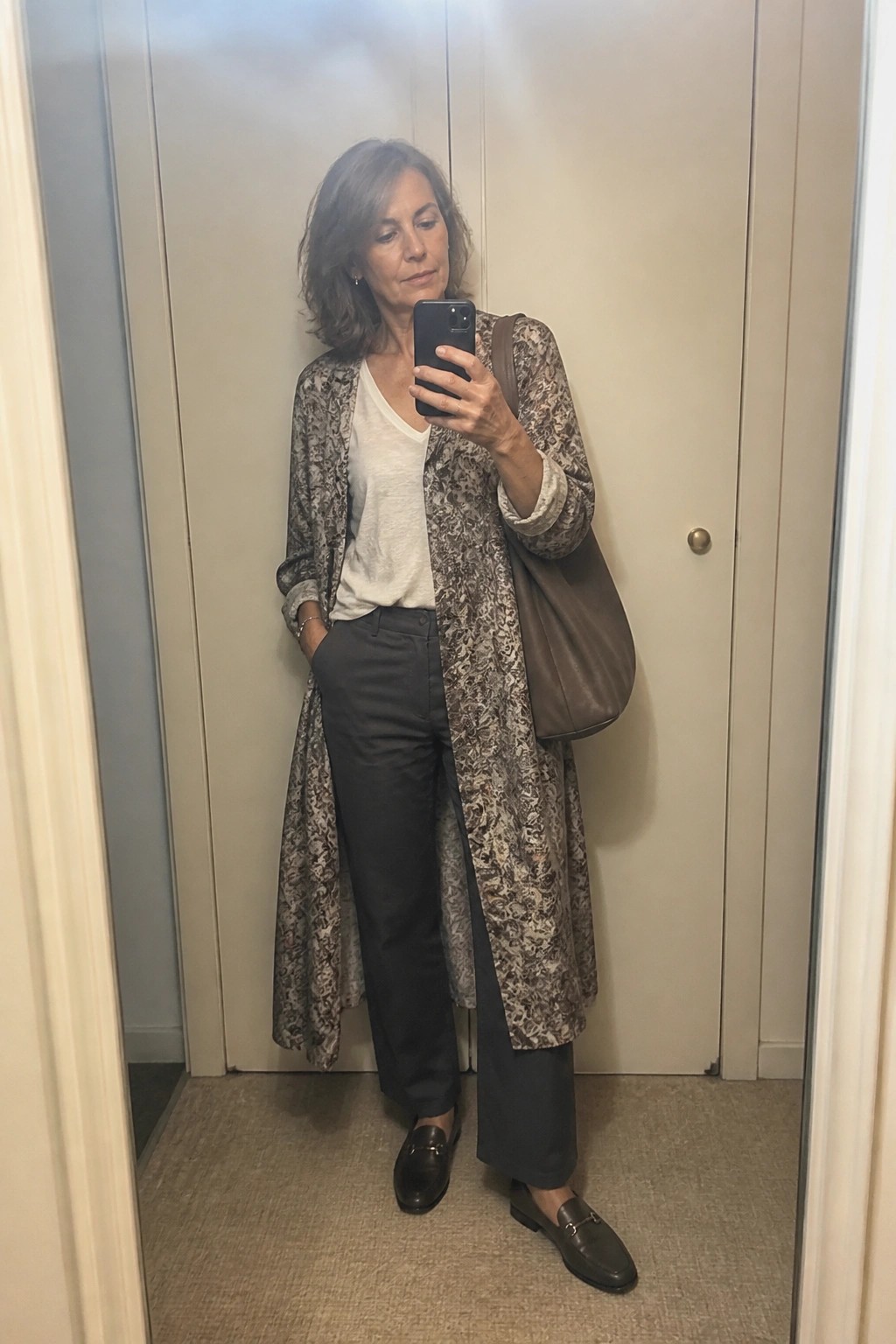Woman with gray hair taking mirror selfie in floral cardigan and dark pants
