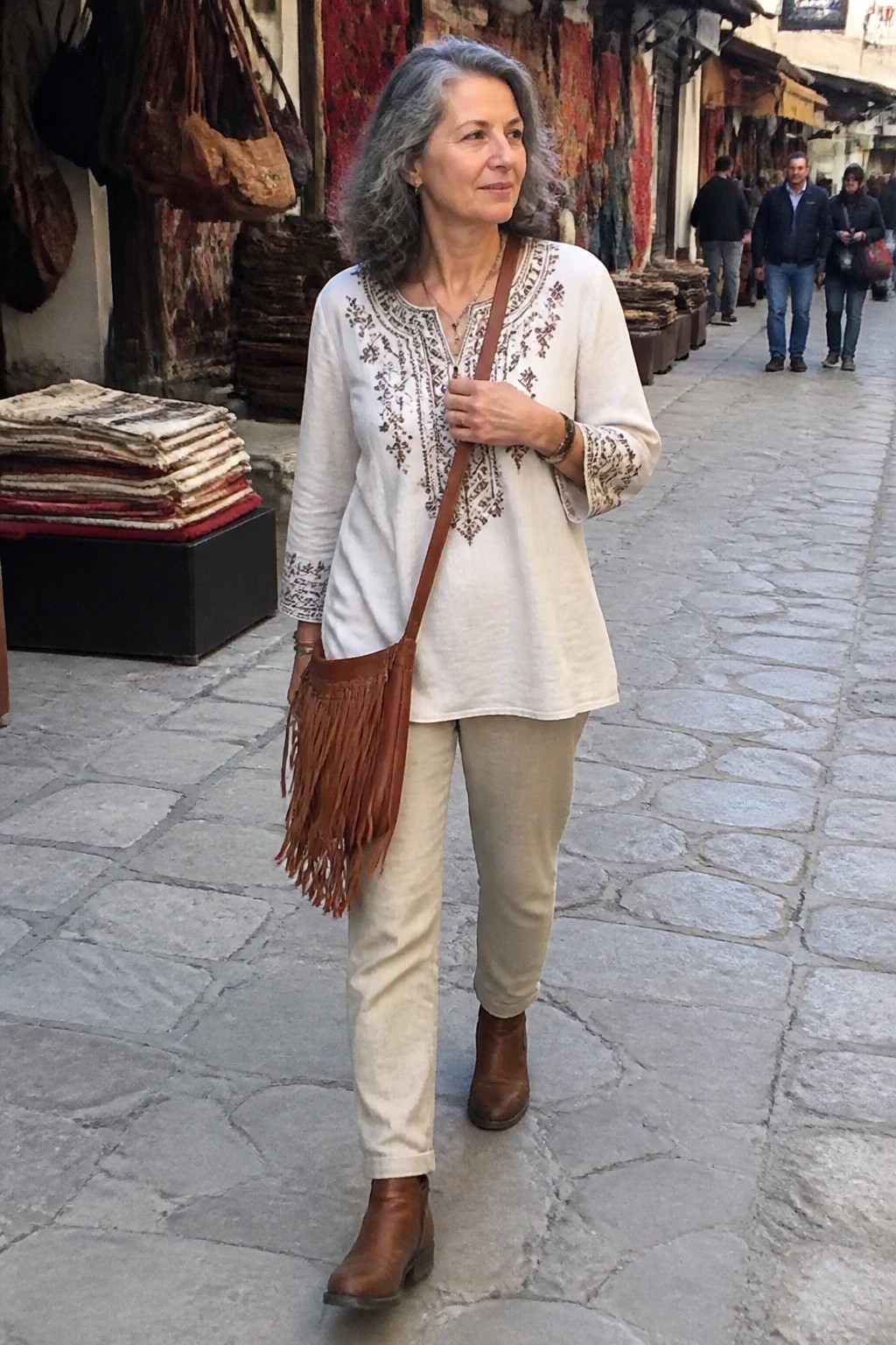 Gray-haired woman in embroidered white tunic with fringed brown bag in rug market alley