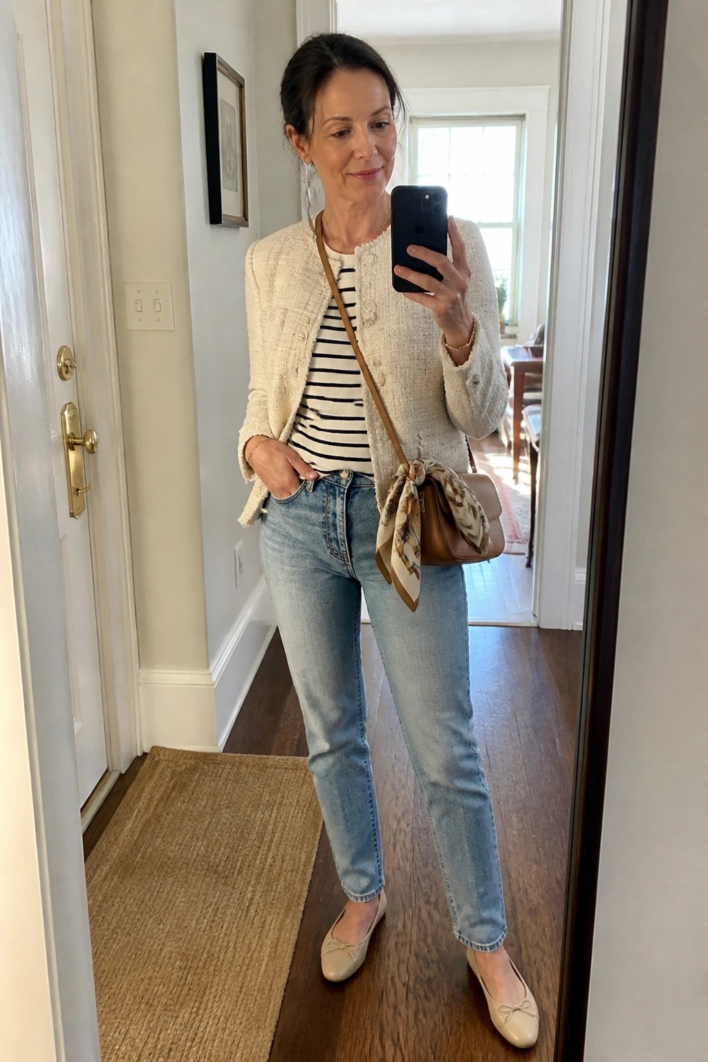 Woman in cream tweed jacket and jeans taking mirror selfie in hallway