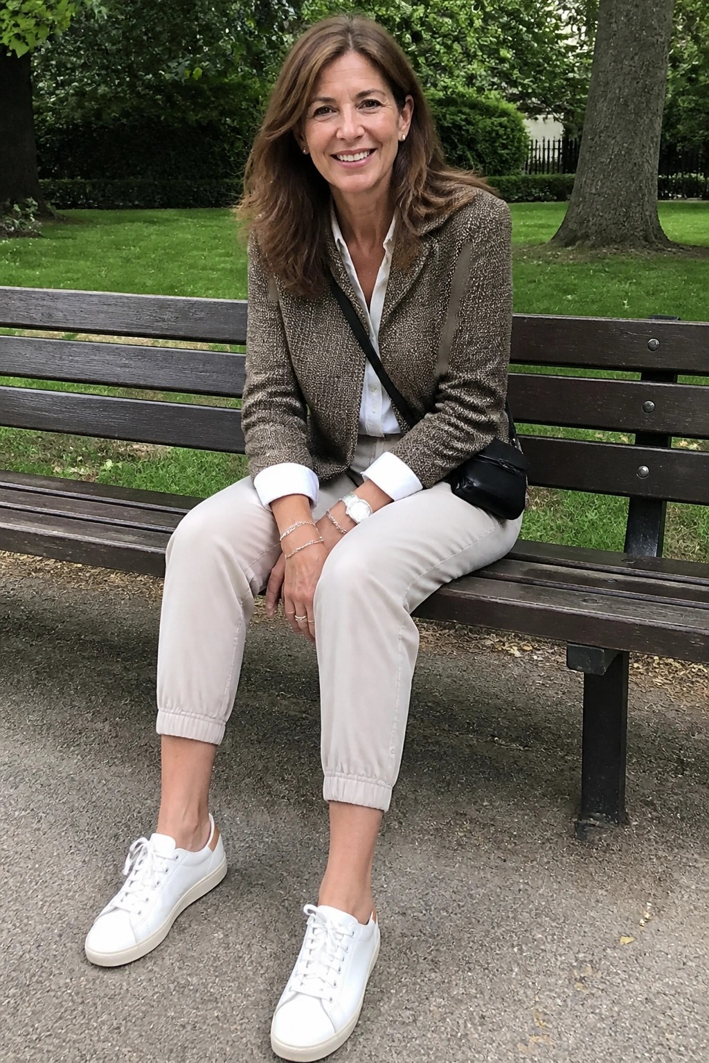 Smiling woman in brown jacket and beige pants seated on wooden park bench