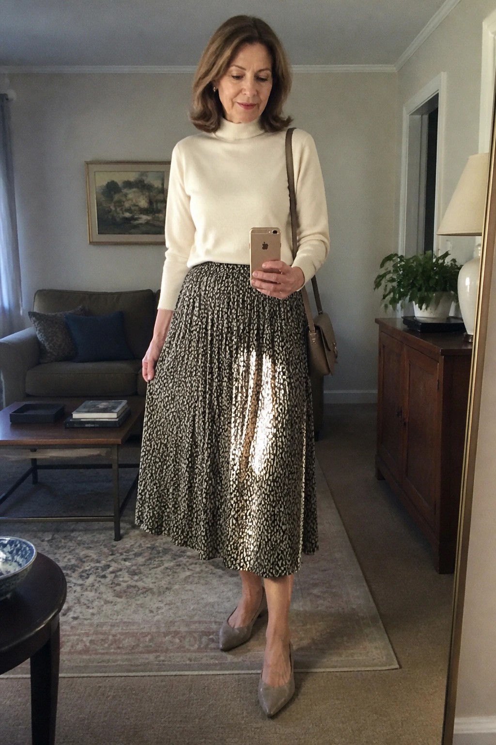 Woman in white turtleneck and shiny patterned skirt checks phone in living room