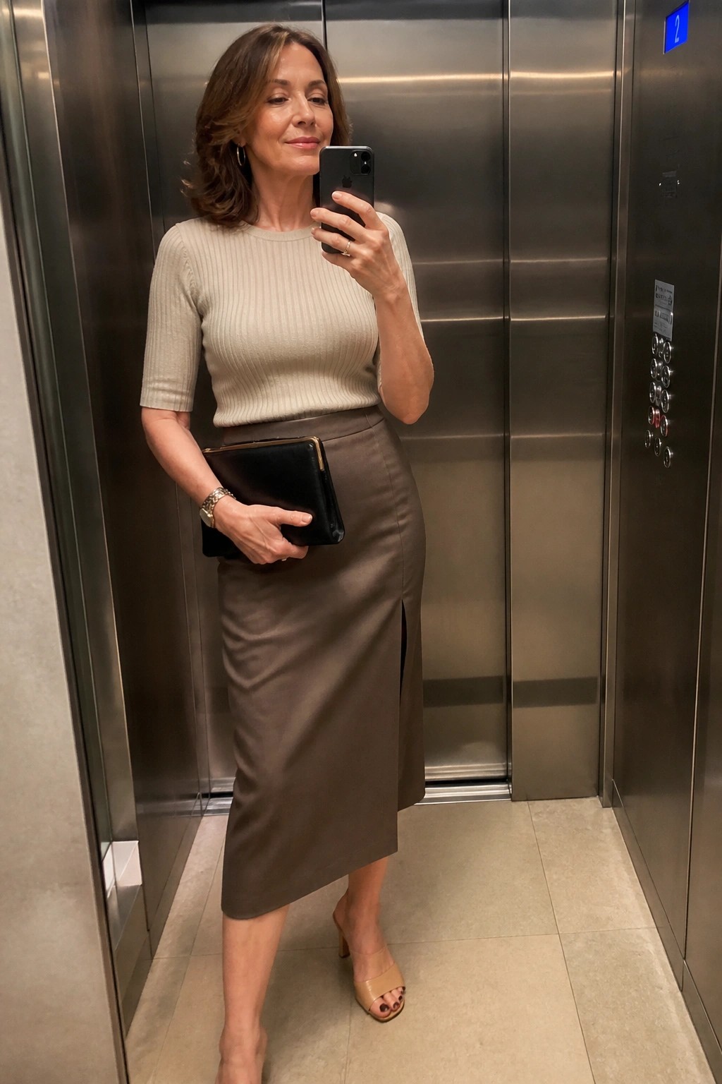 Woman in beige top and brown skirt taking selfie in elevator
