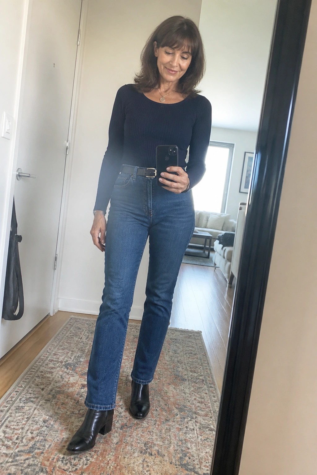 Woman in navy ribbed top and blue jeans takes mirror selfie wearing black boots