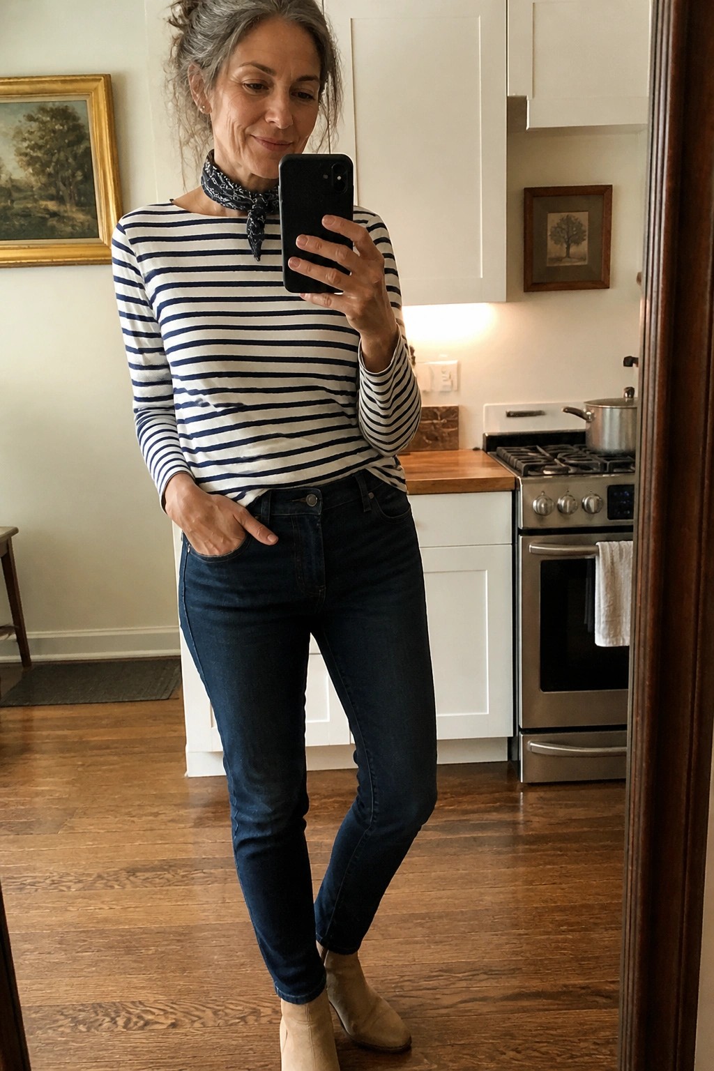 Woman with gray hair in striped shirt and jeans taking kitchen mirror selfie