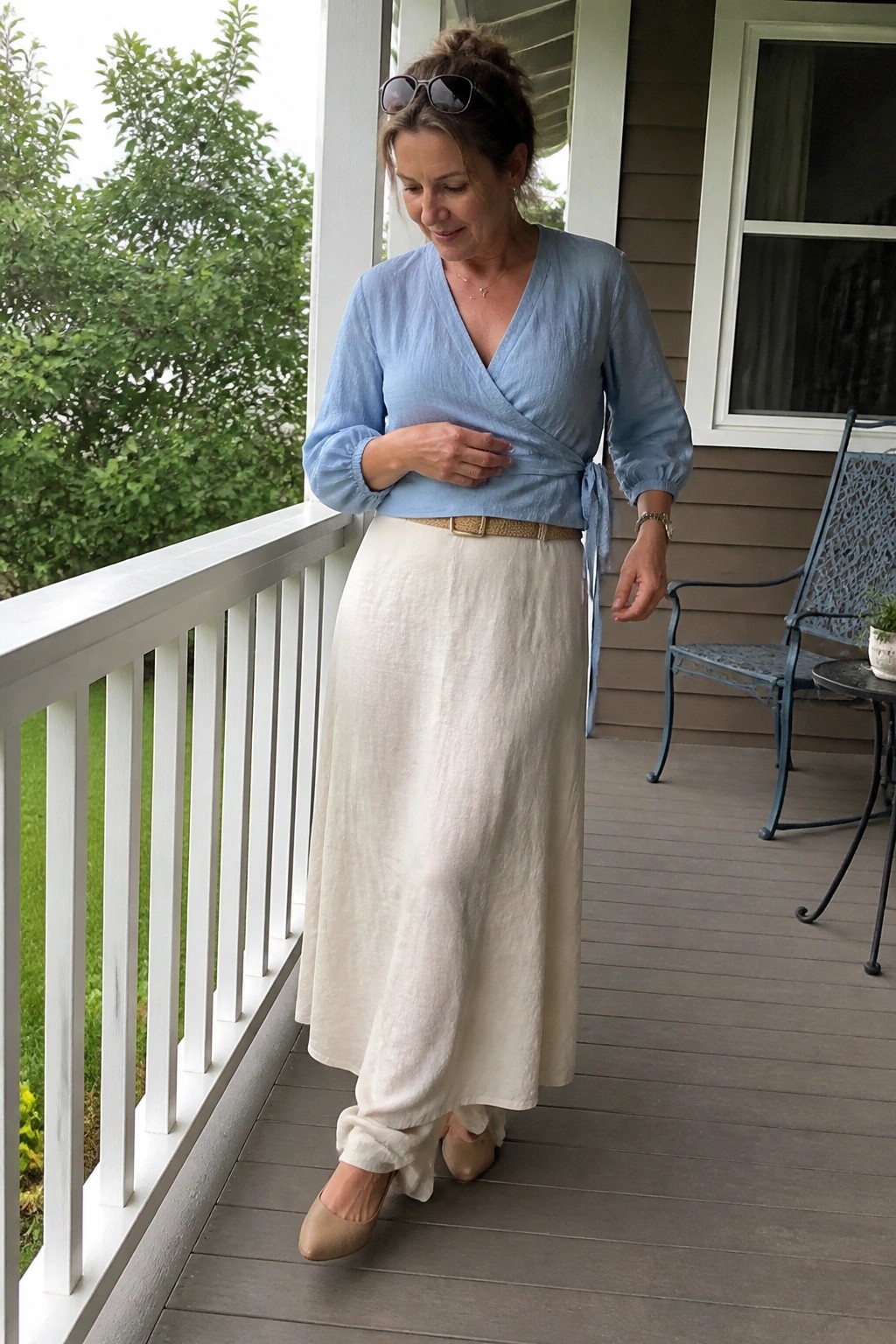 Woman in light blue wrap blouse and cream skirt standing on wooden porch
