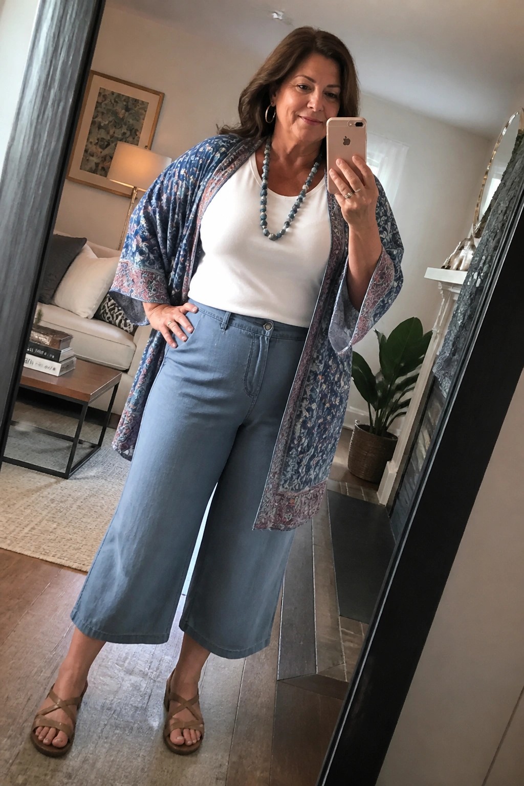 Woman in blue patterned kimono jacket, white top, and wide blue pants taking mirror selfie.
